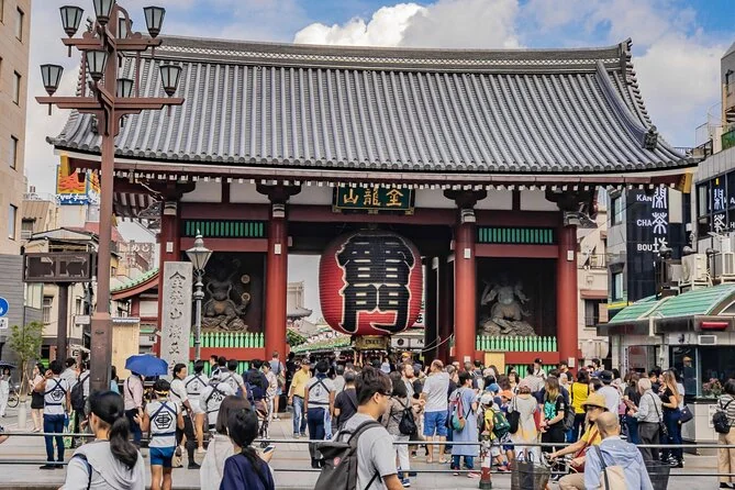 A dense crowd of visitors in front of the Kaminarimon gate and its giant red lantern on a sunny day
