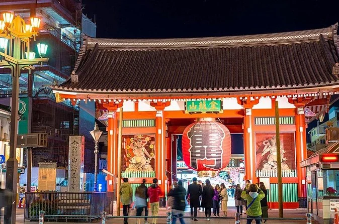 The Kaminarimon gate at night with its red lantern lit and a few people walking past